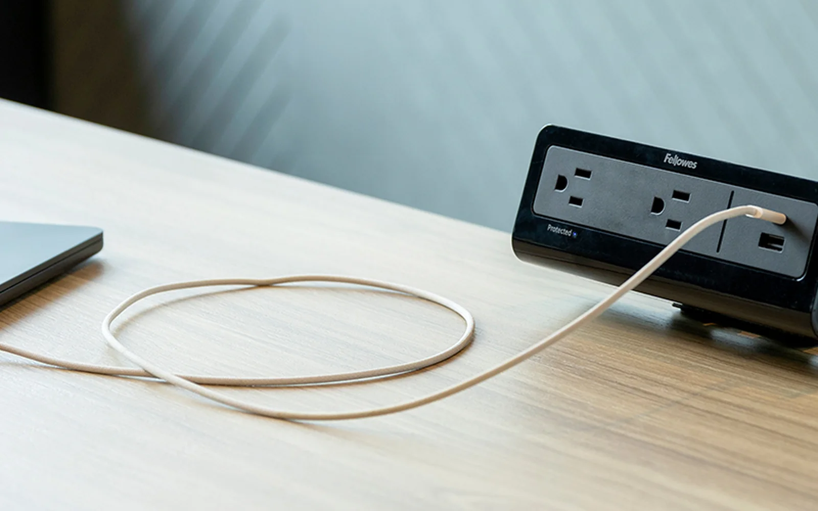 Black Fellowes desktop power unit with outlets and a charging cable on a light wood worksurface