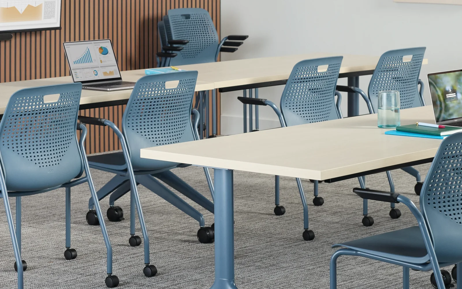 Training room with rectangular tables, rolling chairs, laptops, and presentation screens.