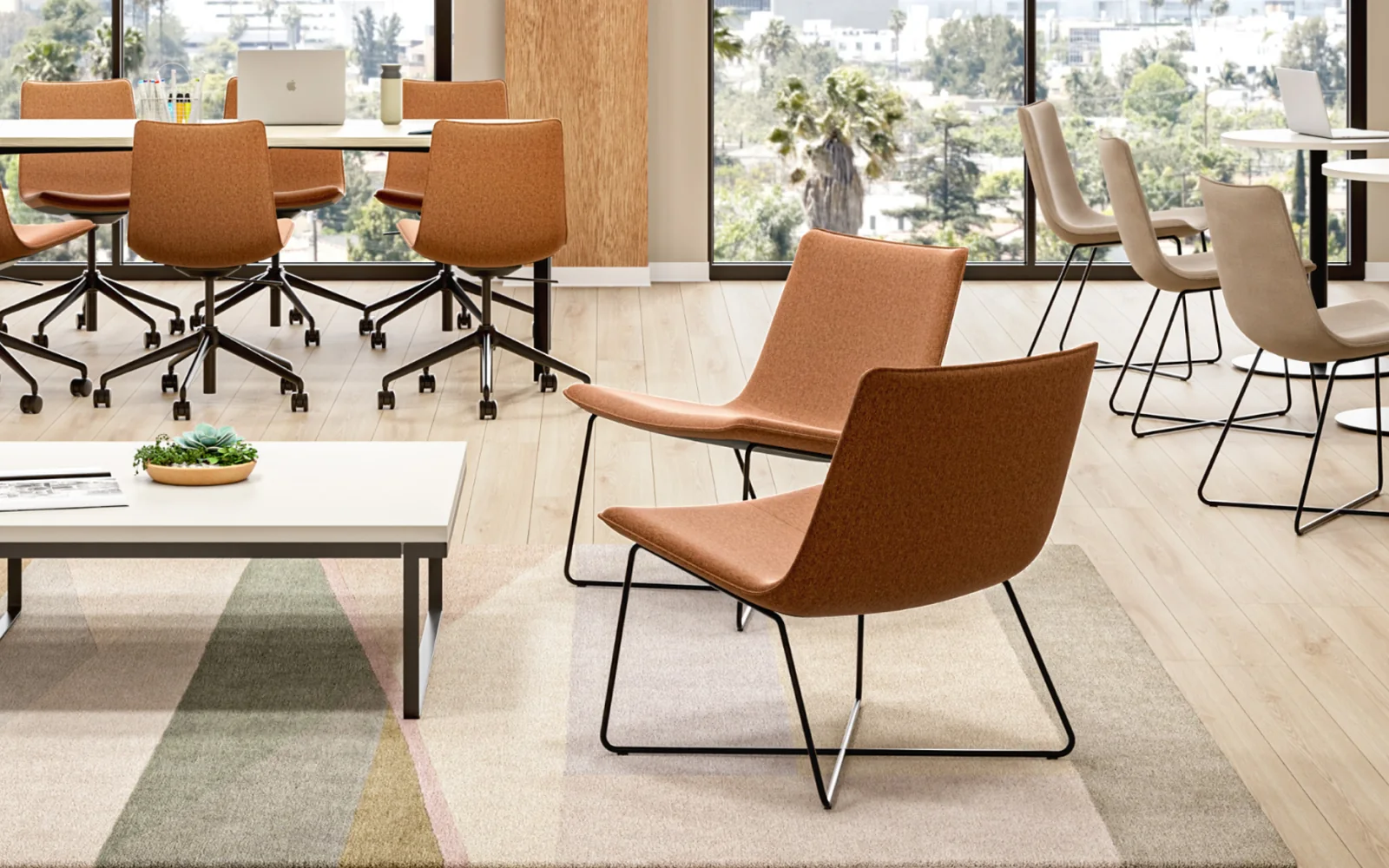 Orange upholstered SitOnIt task and guest chairs arranged around desks and a lounge table in a bright office
