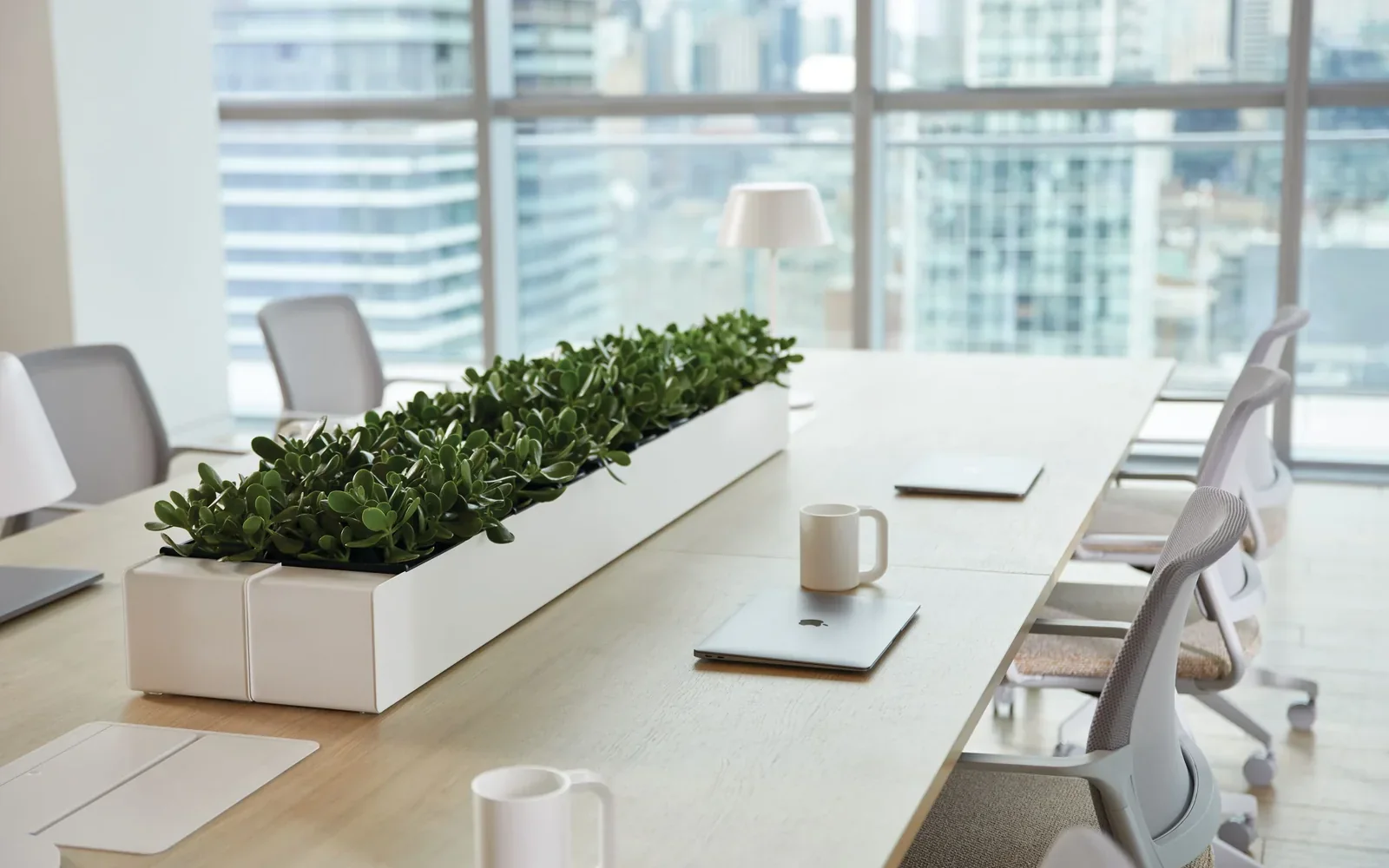 Teknion light-wood meeting table with white office chairs and a long central planter beside floor-to-ceiling windows